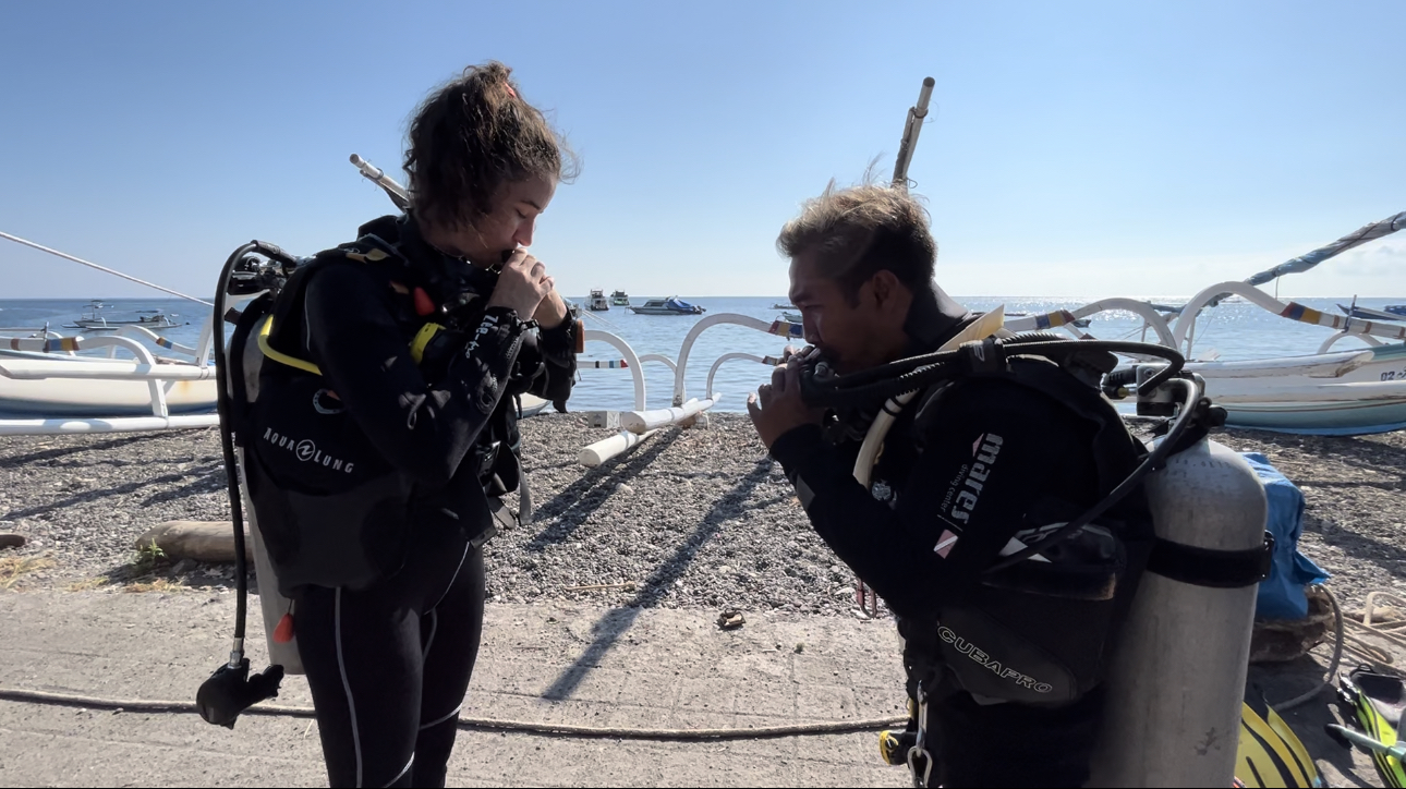 Instructor Gede and student Eloise checking their BCDs as part of the BWRAF buddy check of the PADI Open Water diver course in Amed, Bali
