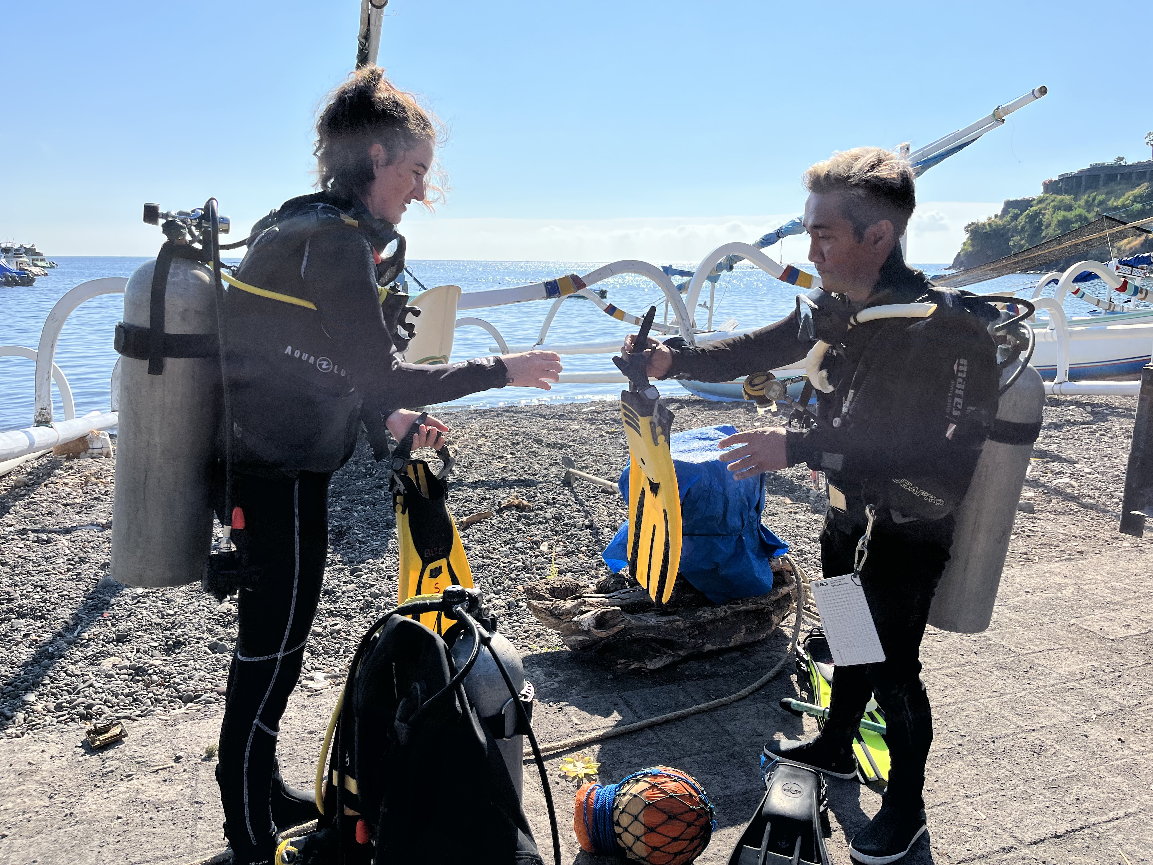 Instructor Gede and student Eloise performing the final check as part of the BWRAF buddy check of the PADI Open Water diver course in Amed, Bali