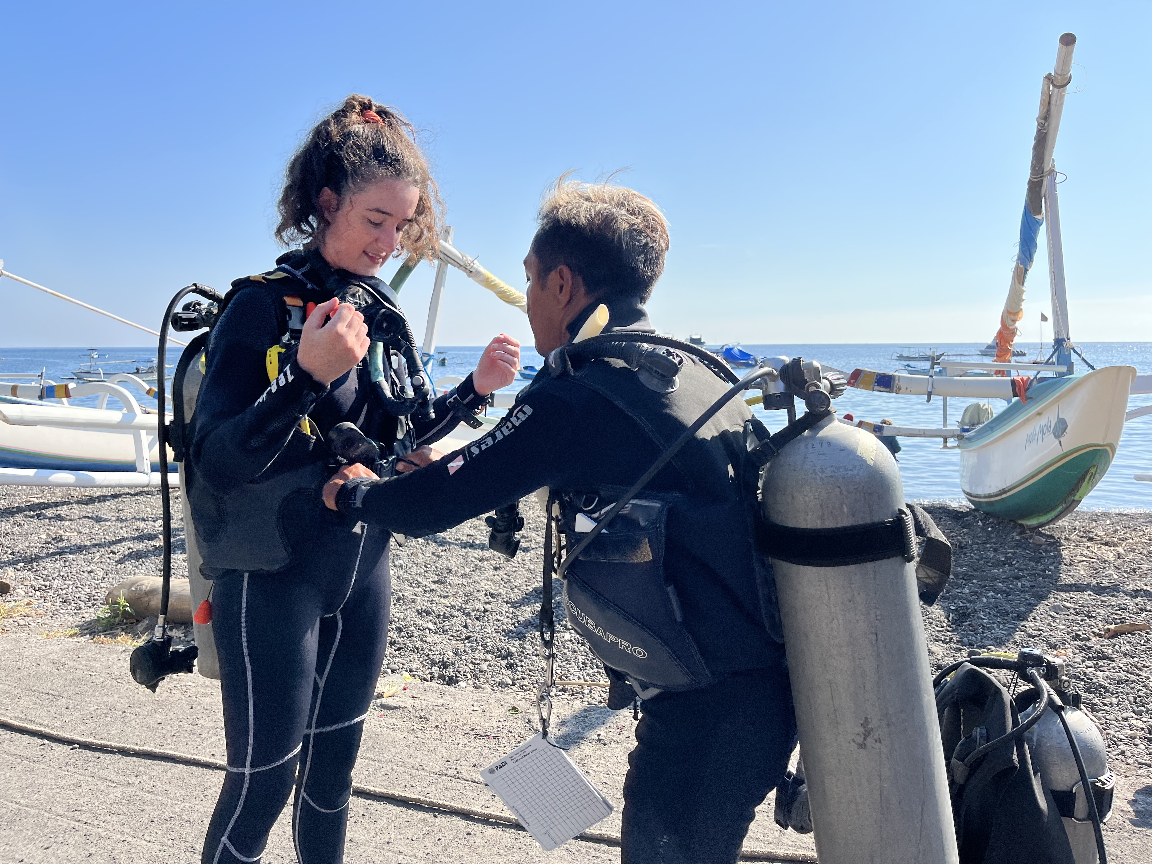 Instructor Gede and student Eloise checking their weight belts as part of the BWRAF buddy check of the PADI Open Water diver course in Amed, Bali