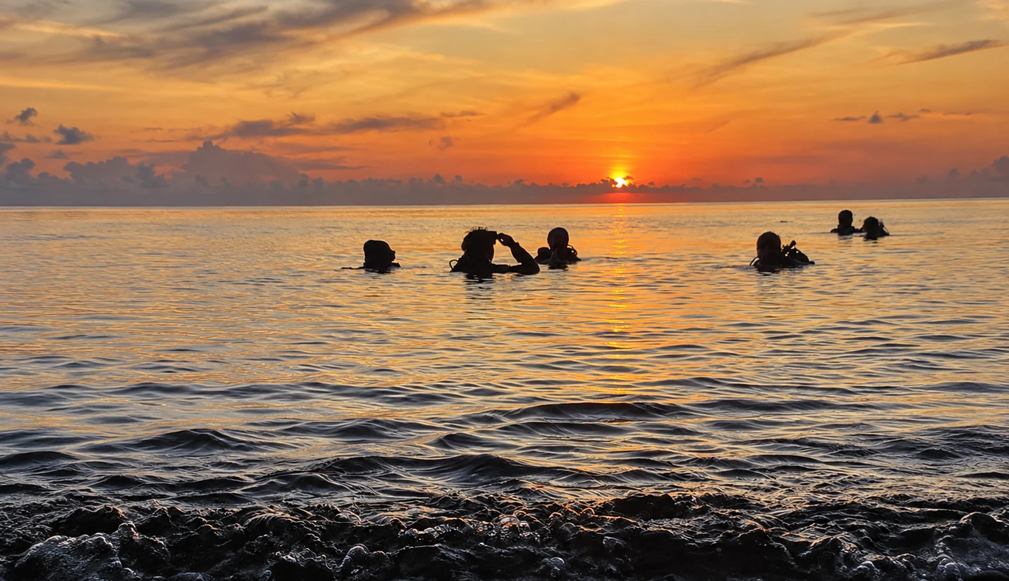 Scuba divers entering calm water at sunrise before a USAT Liberty dive in Tulamben, Bali